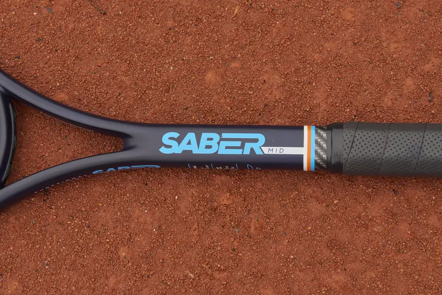 Close-up of the Saber Mid throat and grip, with the Saber logo, on a clay court